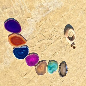 May include: A wind chime made of agate slices in various colors, including purple, red, blue, pink, brown, and green. The slices are suspended from a wooden ring.