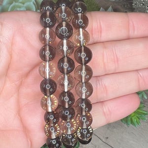 Op de afbeelding: Een bruine rookkwarts kralen armband met meerdere strengen kralen. De kralen zijn rond en hebben een doorschijnende uitstraling.