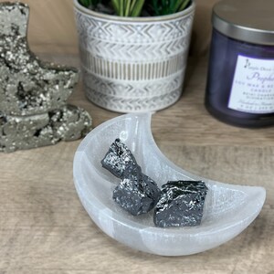 May include: Three pieces of black hematite crystals in a white selenite moon shaped bowl.