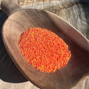 May include: A wooden scoop filled with bright orange, finely chopped pieces. The scoop is made of dark brown wood and has a smooth, curved design. The orange pieces are clustered together, creating a vibrant contrast against the wood.