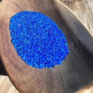 May include: A wooden scoop filled with bright blue glass beads. The beads are small and uniform in size.