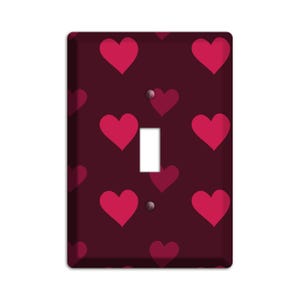 May include: A light switch cover with a dark red background and a pattern of pink hearts.