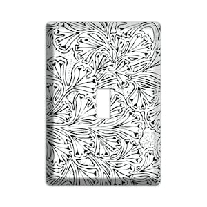 May include: A white light switch cover with a black floral pattern. The design features stylized leaves and vines, creating a symmetrical, artistic look. The cover has a single toggle switch opening.