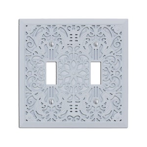 May include: A white, decorative light switch plate with a three-gang design. The plate features a delicate, intricate floral pattern.