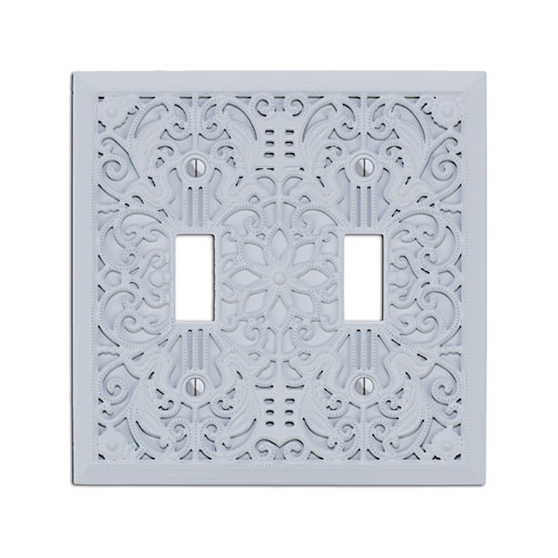May include: A white, decorative light switch plate with a three-gang design. The plate features a delicate, intricate floral pattern.