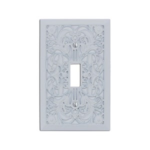 May include: White decorative light switch cover with an intricate floral design.