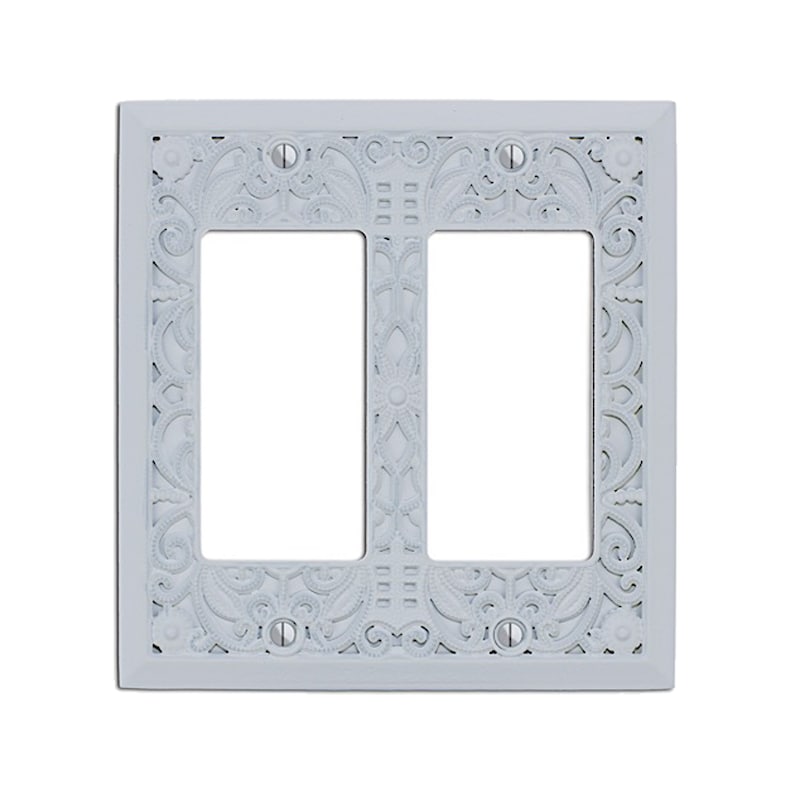 May include: White double-gang wall plate with an ornate, decorative design. The plate has a cutout for two standard electrical outlets.