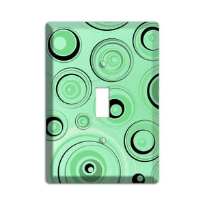 May include: A light green light switch cover with a pattern of black and green concentric circles.