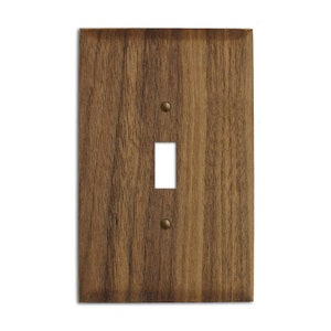 May include: A single-gang light switch cover made of dark brown wood with a wood grain pattern. The cover has two brass screws.