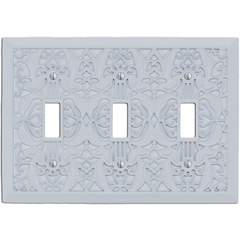 May include: White decorative wall plate with an intricate, embossed design. The plate has three openings for light switches.