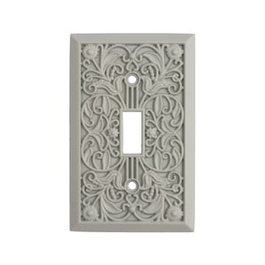 May include: A light gray, ornate switch plate with a single toggle opening. The plate features a detailed floral and leaf design, with a rectangular frame. The design is symmetrical, with a classic, vintage aesthetic.