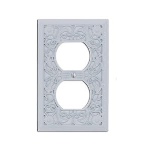 May include: White decorative outlet cover with an ornate, floral design.
