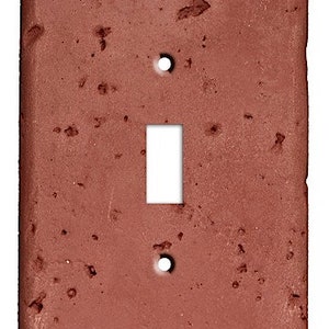May include: A single-gang light switch cover made of terracotta with a rough, textured surface. The cover is a reddish-brown color.