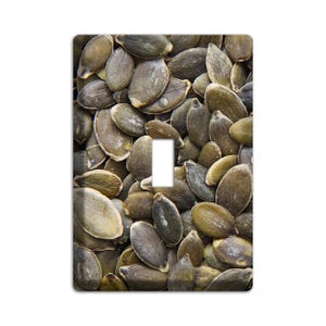 May include: A light switch cover featuring a close-up image of a pile of pumpkin seeds.