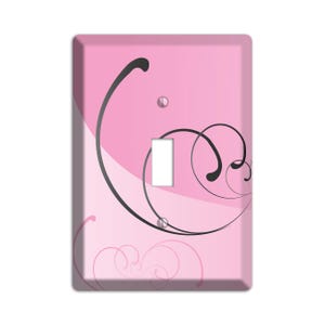 May include: Pink light switch cover with a black swirl design.