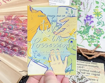 May include: A small, yellow, green, and blue illustrated book with the title "Live in Possessions: writings about long distance and co-habitation" by Ghost Dandy and Co.