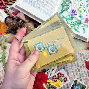 May include: A set of gold communication cards with blue accents and the text "Communication Cards" printed on the front. The cards are held in a hand.