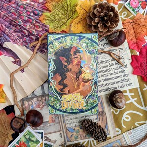 May include: A tarot card with a green, blue, and gold border. The card features a woman with pointed ears and long brown hair. She is holding a glowing orb in her hand. The card is titled "Oracle Diviner".