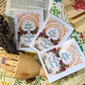 Könnte beinhalten: Drei kleine Karten im Vintage-Stil mit einem floralen Design und dem Text "A Brief Thought On The Language of Tieflings".