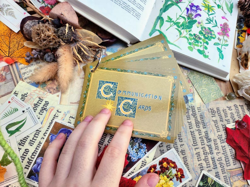 May include: A set of gold-colored communication cards with a blue and gold logo that says "Communication Cards". The cards are fanned out and held by a hand.