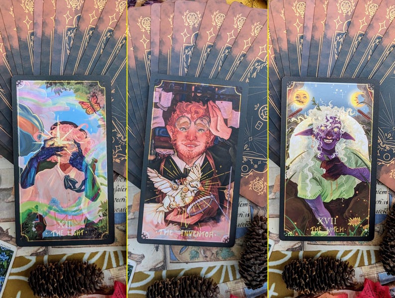 May include: Three tarot cards with black borders and gold accents. The first card shows a person with a rainbow halo holding a glowing orb. The card is titled "The Light". The second card shows a person with red hair and a beard holding a bird. The card is titled "The Inventor". The third card shows a person with green skin and white hair holding a flower. The card is titled "The Witch".