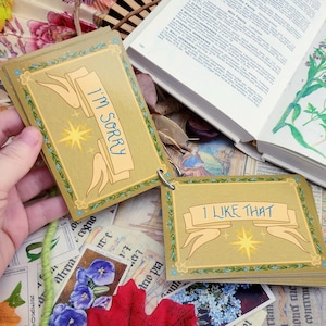 May include: A set of small cards with gold backgrounds and green borders. The cards have a star and a banner with the text "I'M SORRY" and "I LIKE THAT" on them.