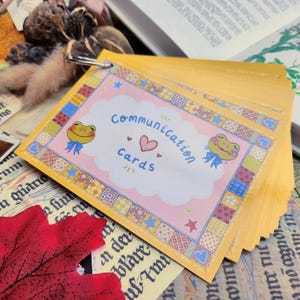 May include: A stack of yellow communication cards with a pink and white design featuring a frog and the text "Communication Cards".