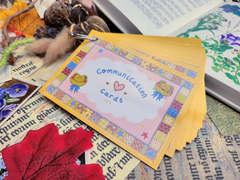 May include: A stack of yellow communication cards with a pink and white design featuring a frog and the text "Communication Cards".