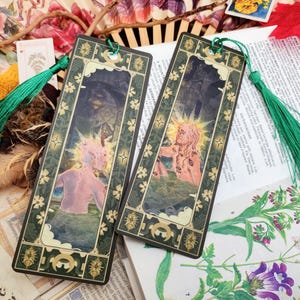 Peut inclure: Deux glands de marque-page verts avec un fond vert foncé. Les marque-pages présentent une bordure dorée et verte avec un motif floral. L'image sur le marque-page représente une personne avec une auréole de lumière et un fond de forêt.