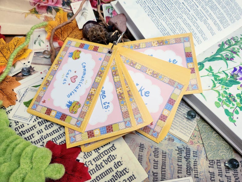 May include: A set of pink and yellow communication cards with a patchwork design. The cards feature a frog and the text "Communication Cards" and "me is:"