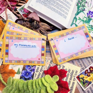 May include: A set of colorful cards with a pink and yellow patchwork design. The cards have a white cloud shape with the text "my pronouns are:" and "i have..." written in black marker.