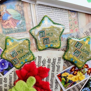 May include: Three green star-shaped pins with embroidered text. The pins say "Any Pronouns", "They Them", and "Please Ask".