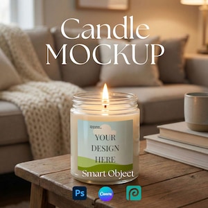 May include: A lit candle in a clear glass jar with a label that reads "YOUR DESIGN HERE" and "Smart Object." The candle sits on a wooden table with books and a mug nearby. The background includes a couch and the text "Candle MOCKUP."