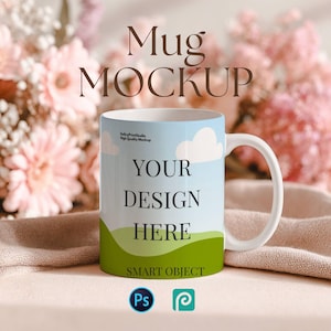 May include: White ceramic mug with a handle, featuring a sky and cloud design with the text "YOUR DESIGN HERE". The mug is set against a backdrop of pink flowers and a beige cloth. The words "Mug MOCKUP" are at the top.
