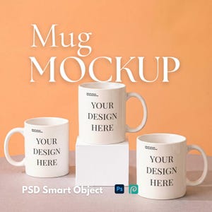 May include: Three white ceramic mugs arranged for display, each featuring the black printed text 'YOUR DESIGN HERE' on the front. The central mug is elevated on a white square block, while the other two sit on the surface. The text 'Mug MOCKUP' appears above.