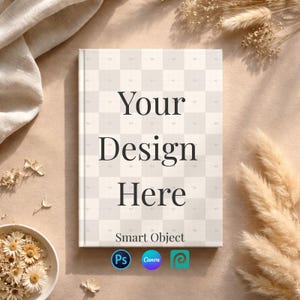Puede incluir: Maqueta de libro de tapa dura con el texto "Your Design Here" en fuente serif. La portada tiene un patrón de cuadros beige claro. El libro está rodeado de flores secas y un cuenco de margaritas secas. La parte inferior del libro tiene las palabras "Smart Object" y tres logotipos de aplicaciones.