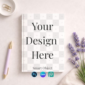 Op de afbeelding: Een hardcover notitieboek met de tekst "Your Design Here" op een geruit patroon. Een lavendelkleurige pen, een klein kommetje met paperclips en takjes lavendel zijn rond het notitieboek gerangschikt. Het notitieboek heeft het "Smart Object" logo en de logo's voor Photoshop, Canva en PicMonkey.