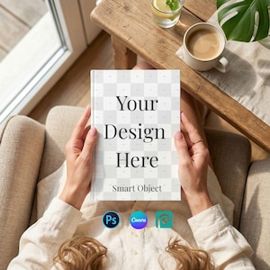 以下が含まれることがあります： 「Your Design Here」と「Smart Object」のテキストが入った本が人に持たれています。本はチェック柄の表紙です。画像には、飲み物とコーヒーカップが置かれた木製のテーブルも写っています。