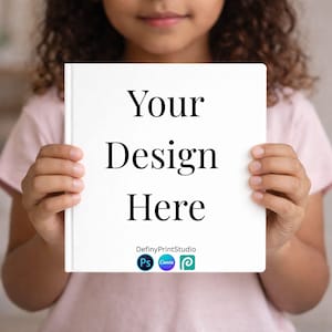 May include: A white book cover with the text "Your Design Here" in a bold, black font. The book is held by a person. The bottom of the cover features the text "DefinyPrintStudio" and three app logos: Photoshop, Canva, and a green logo.