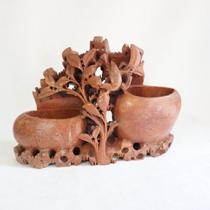 Könnte beinhalten: Eine handgeschnitzte Skulptur aus rotem Stein, die einen Baum mit zwei Schalen darstellt. Der Baum ist aufwendig mit Blättern und Blüten geschnitzt. Die Schalen sind rund und haben eine glatte Oberfläche.