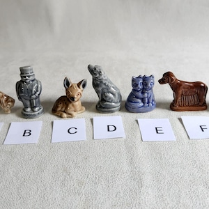 May include: A set of seven miniature ceramic figurines, each depicting a different animal. The figurines are arranged in a row from left to right, labelled A through G. The figurines are painted in various shades of blue, brown, and grey.