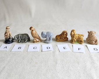 Może przedstawiać: Zestaw dziewięciu miniaturowych figurek ceramicznych, z których każda przedstawia inne zwierzę. Figurki są ułożone w rzędzie od lewej do prawej, oznaczone literami od A do I. Figurki są pomalowane w różnych odcieniach brązu, szarości i błękitu.