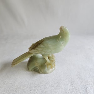 May include: A green jade carving of a bird perched on a branch. The bird is detailed with intricate carvings and has a long tail.