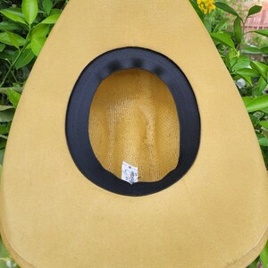 Op de afbeelding: Een beige strooien cowboyhoed met een zwarte band rond de kroon. De hoed heeft een geweven textuur en een label aan de binnenkant met de tekst "Stetson".