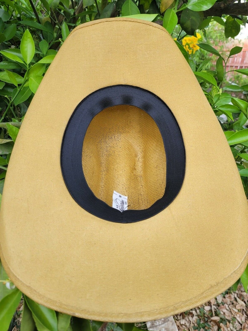 Op de afbeelding: Een beige strooien cowboyhoed met een zwarte band rond de kroon. De hoed heeft een geweven textuur en een label aan de binnenkant met de tekst "Stetson".