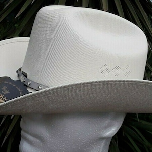 May include: A white cowboy hat with a silver band and a black label that says "The Best Stain" on it.