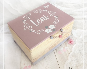 Könnte beinhalten: Eine rosafarbene Holzkiste mit einem Blumengirlanden-Design und dem Namen "Leni" in weißen Buchstaben. Die Kiste hat einen Holzgriff mit grauen und rosa Perlen.