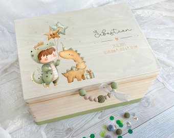 May include: A rectangular wooden keepsake box with a light wood finish and a green base. The lid features a printed illustration of a child in a dinosaur costume and a cartoon dinosaur with balloons. Text includes the name Sebastian and birth details.