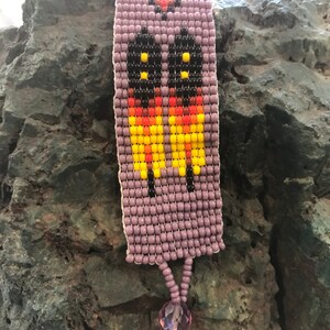 May include: A purple beaded bracelet with a colorful geometric design. The bracelet has a small purple crystal charm at the end.
