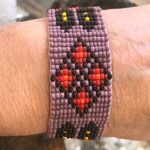May include: A beaded bracelet with a geometric pattern in shades of purple, black, orange, and red.